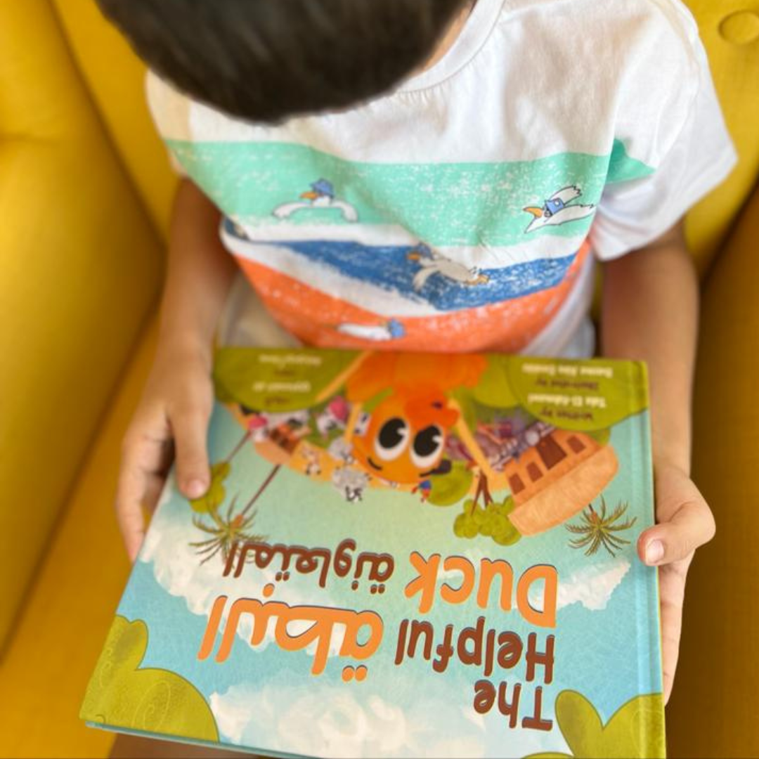 Child sitting on a yellow chair holding The Helpful Duck bilingual Arabic-English book, featuring a bright and playful cover illustration